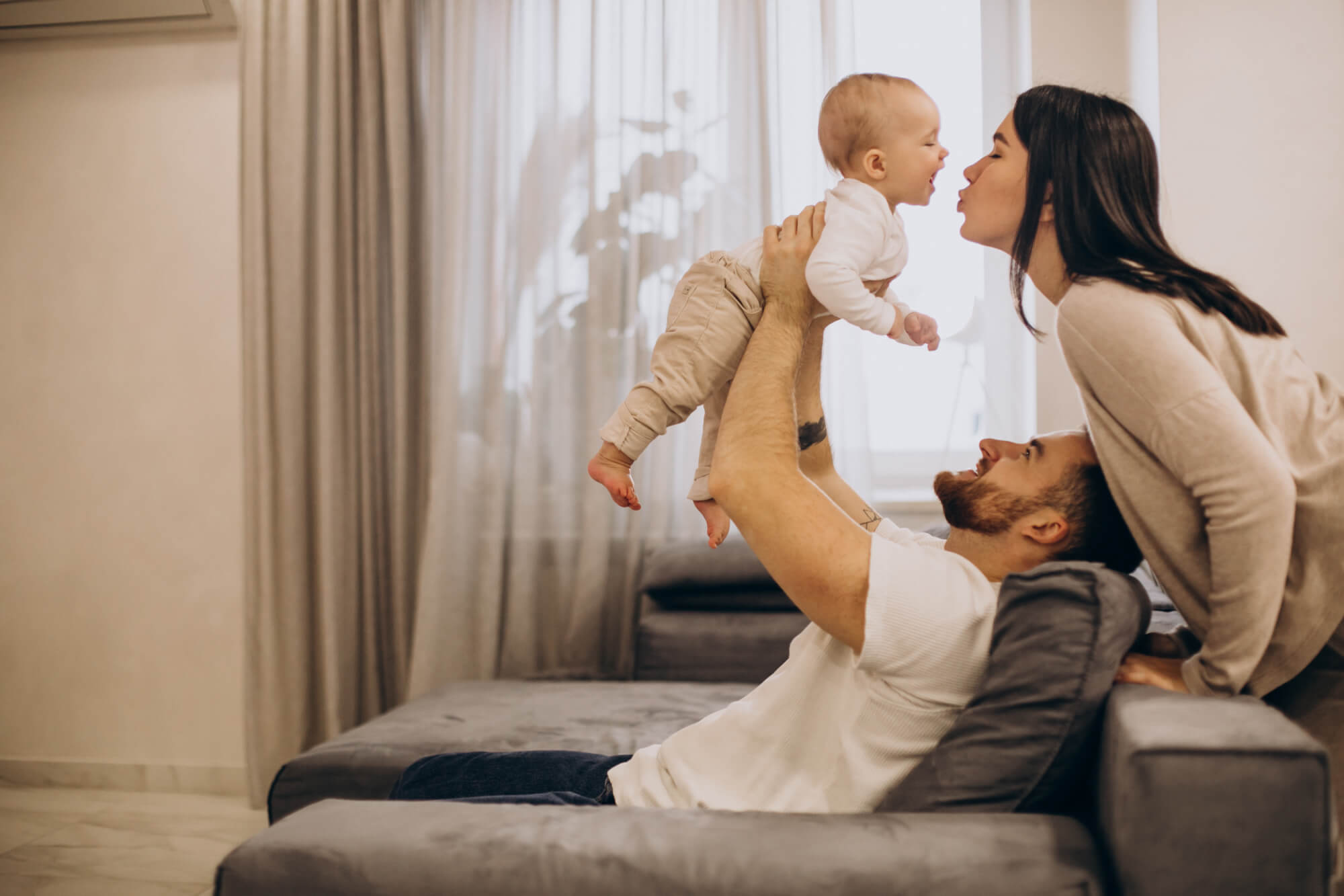 Young Family With Toddler Baby Daughter Sitting On Coach At Home