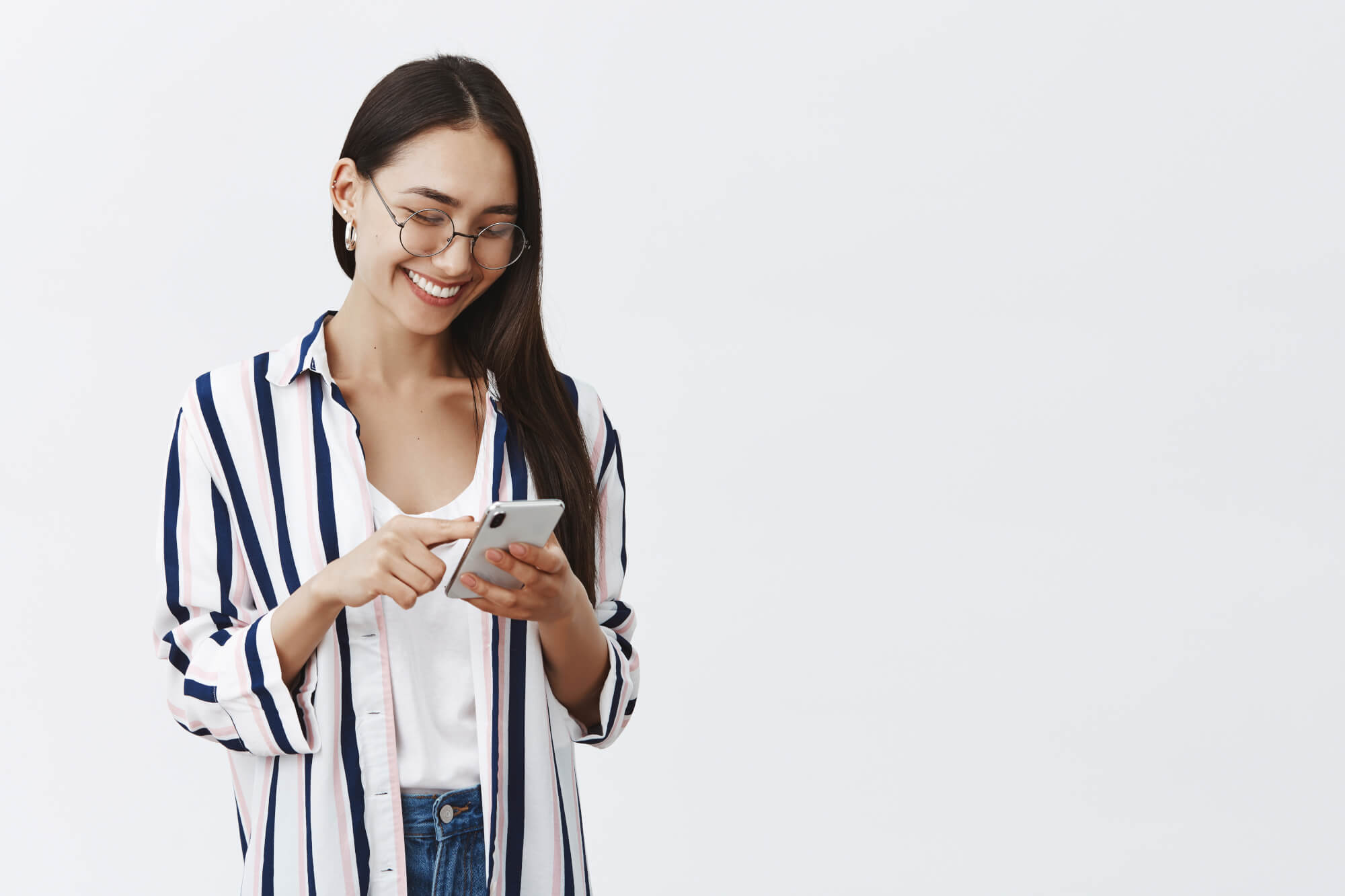 Choosing New Wallpaper On Smartphone. Portrait Of Happy Attractive And Stylish Woman In Glasses And Striped Blouse Scrolling Feed While Using Smartphone, Reading Amusing Article In Internet